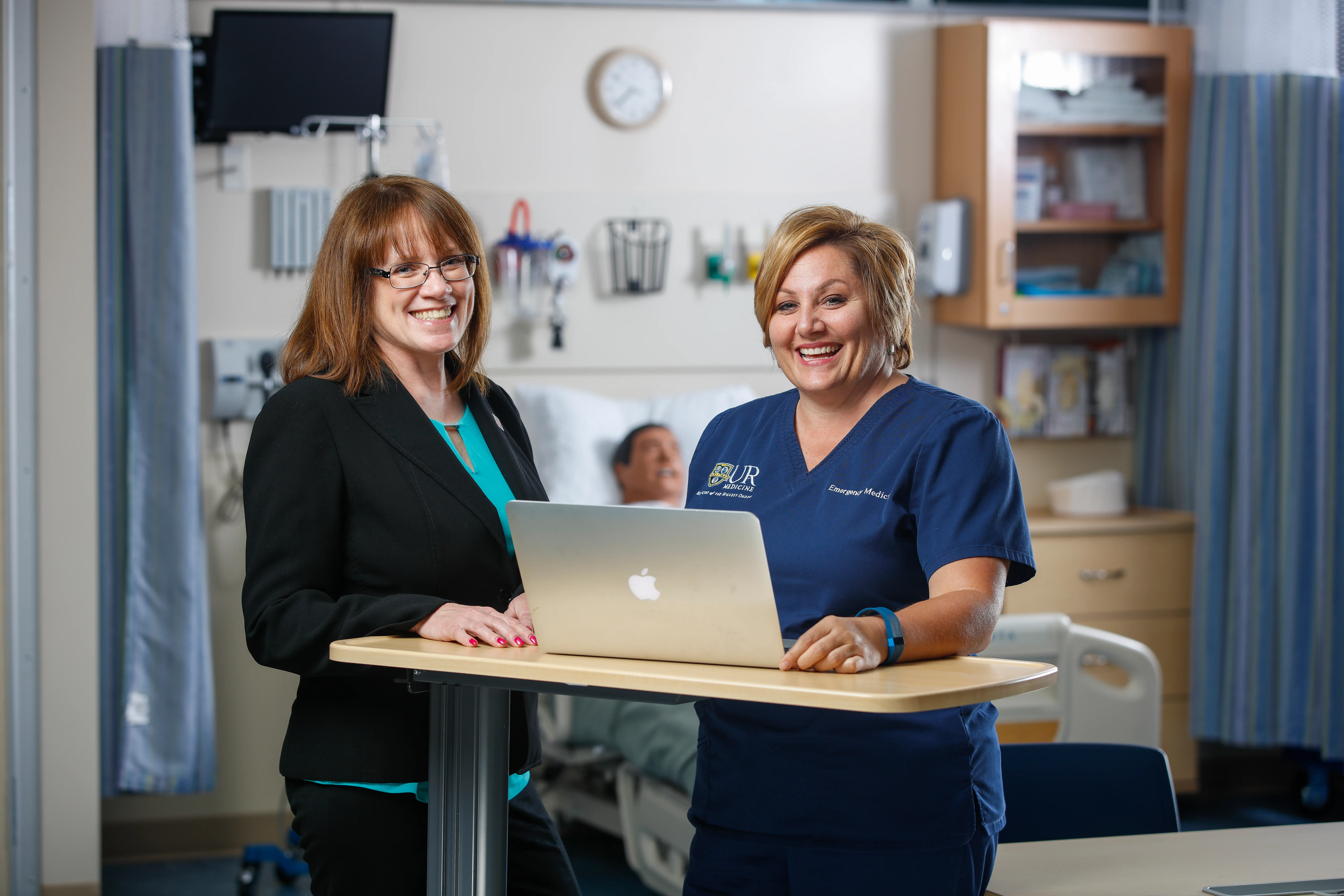 A nurse and nurse leader smile and stand together.