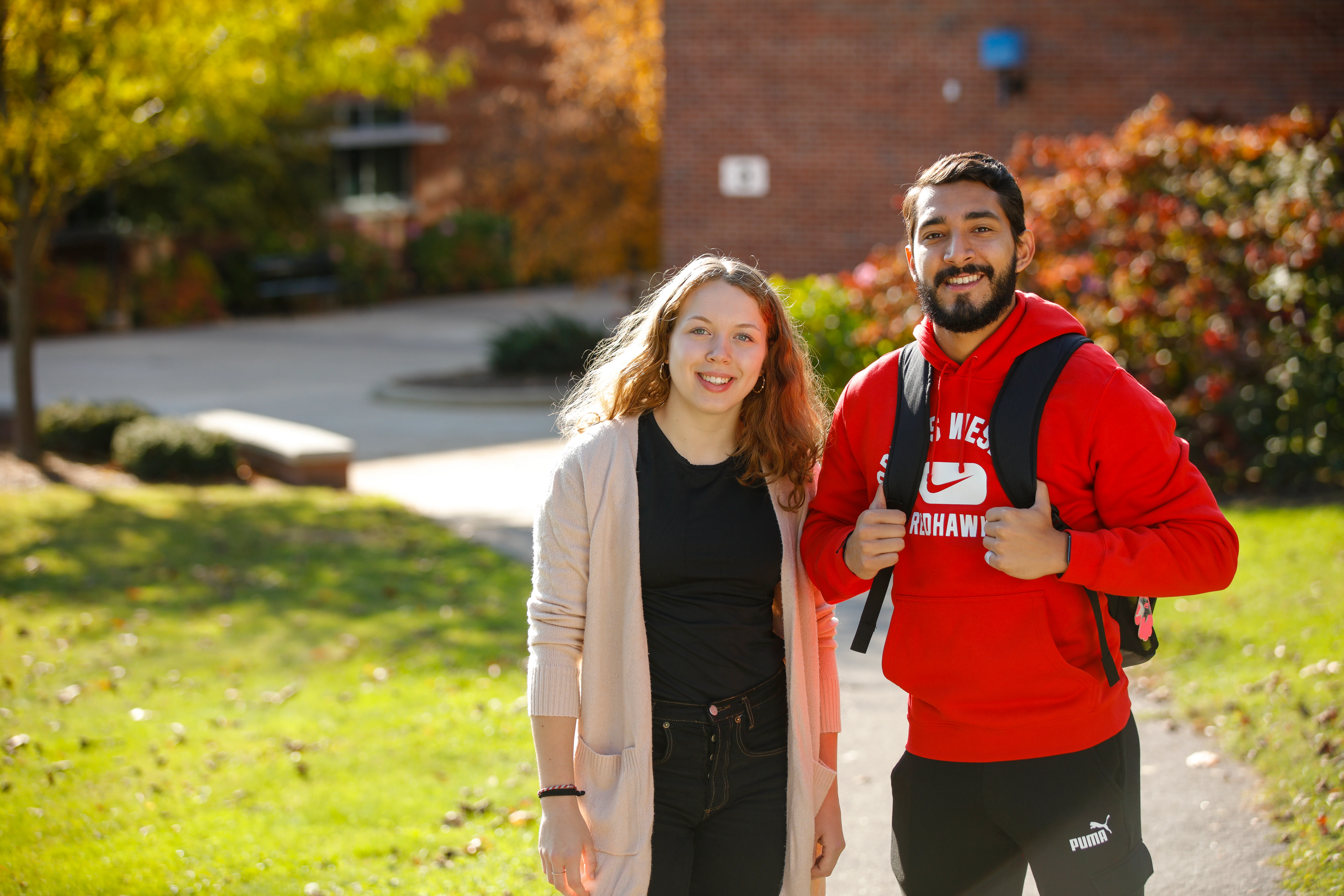 A young man and woman stand on campus and smile
